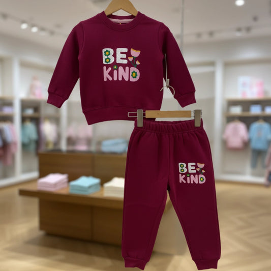 Maroon children's sweatshirt and pants set with 'BE KIND' text on a hanger in a store setting.